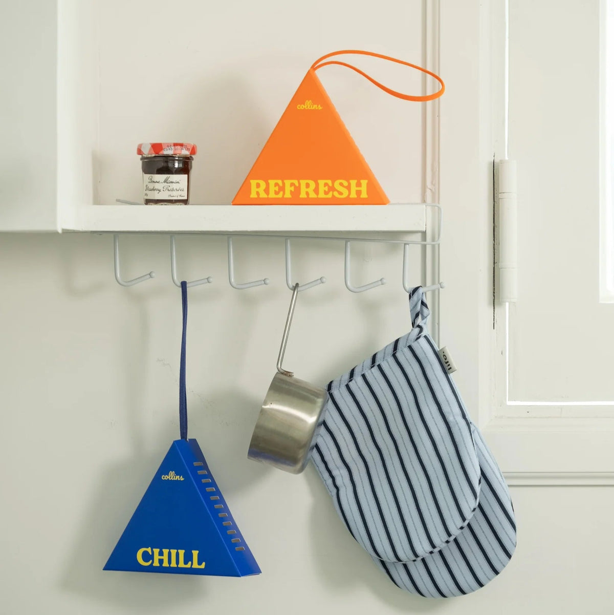 Decorative items including a blue cone labeled 'CHILL', an orange cone labeled 'REFRESH', and a striped oven mitt hanging on a white wall with hooks.