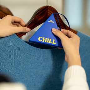 Person holding a blue triangle fragrance sachet with 'CHILL' text on a hanger with a blue sweater.