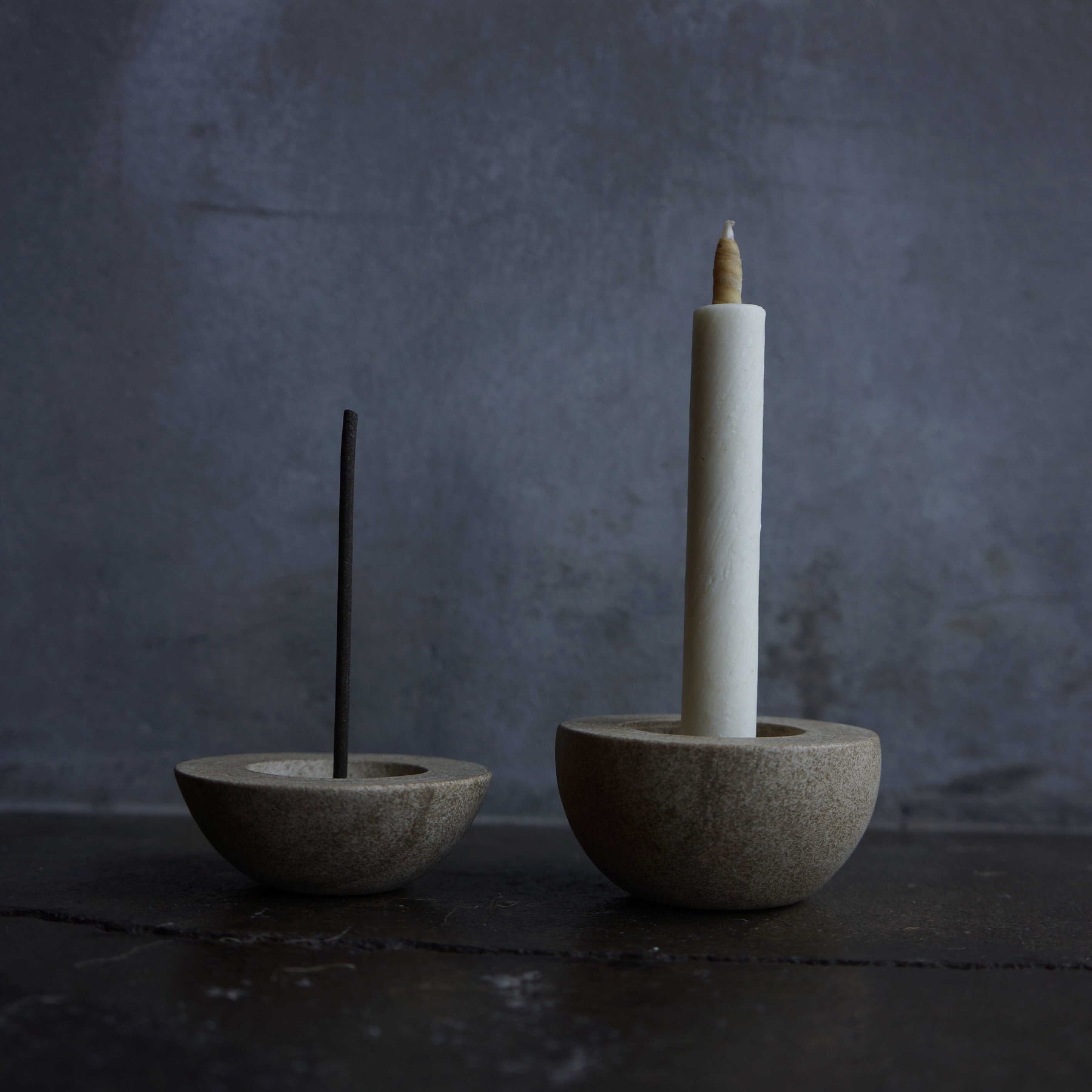 Two concrete incense holders with sticks on a dark surface and background