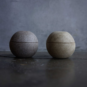 Two spherical stone containers on a dark surface with a gray background