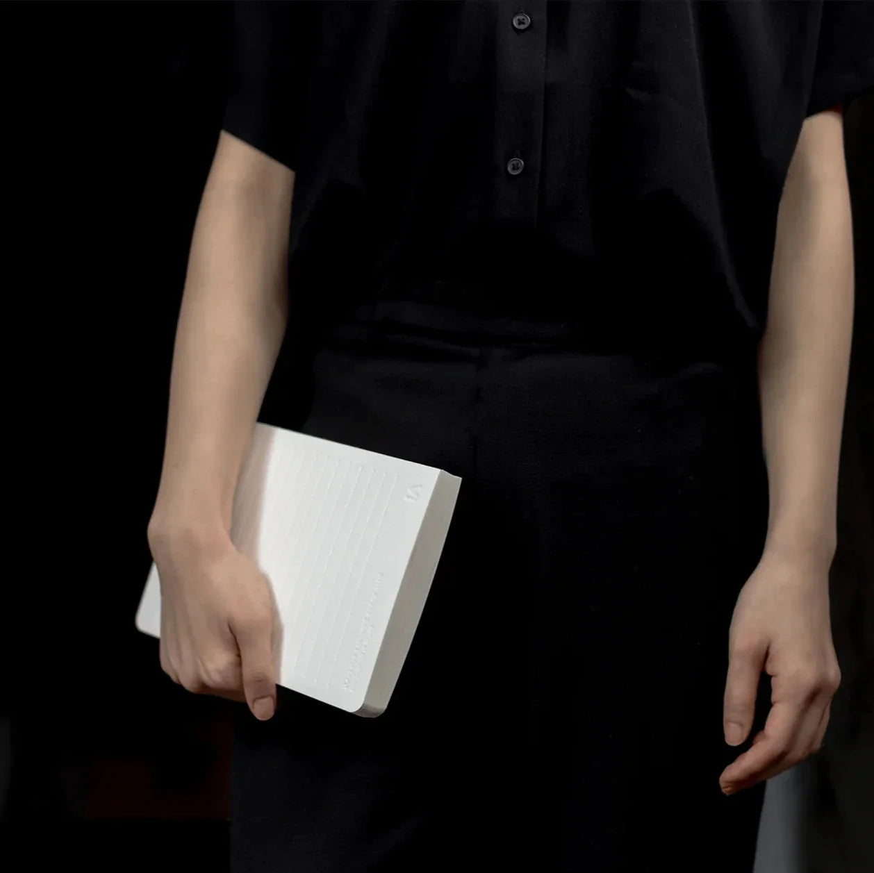 Person holding a white book against a dark background