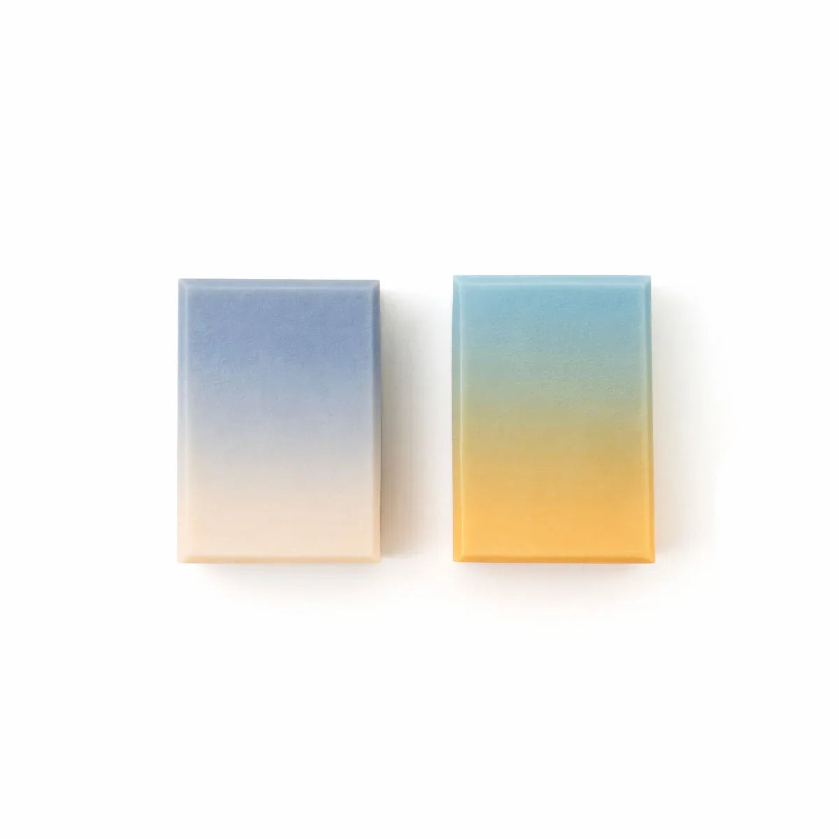 Two small rectangular gradient tiles of soap on a white background, one fading from blue to cream and the other from blue to yellow.