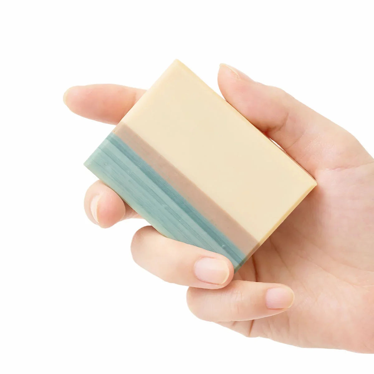 A hand holding a rectangular bar of soap with a cream-colored top half and a light blue-green bottom half, isolated on a white background.